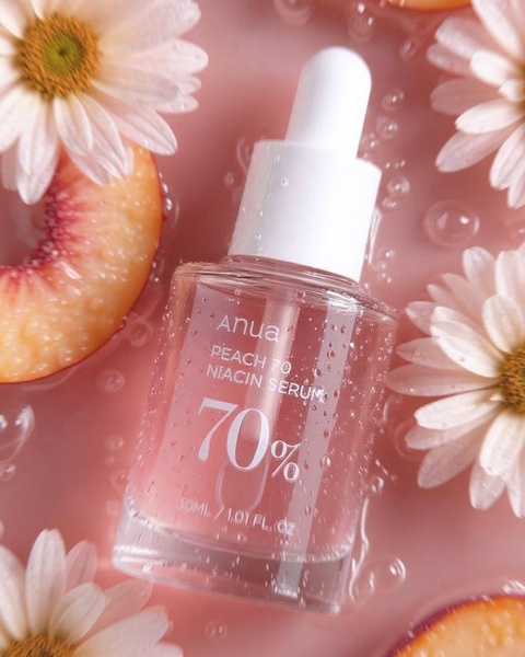 A high-quality product shot of a facial serum bottle surrounded by fresh peach slices and daisy petals in a wet, soft-focus environment.